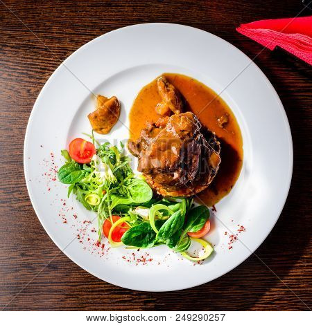 Meat Dish. Appetizing Beef Cheeks In Sauce With Tomatoes And Basil Leaves In A Restaurant. Top View,
