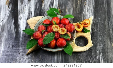 Red Sweet Plums With Green Leaves On A Plate And A Wooden Board On A Dark Background. Flat Lay, Spac