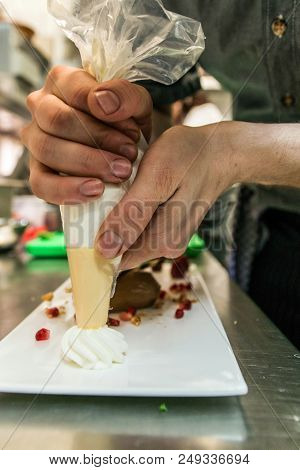 Cook Adding Cream To A Piece Of Brown Mousse Au Chocolate Sweet Dessert And Decoration On A White Pl