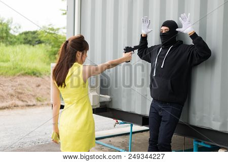 A Woman Pointing A Gun To A Villain Who Wear Black Mask And Black Clothes. The Villain Raised Both H