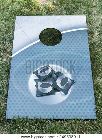 An Metal Aqua Colored Corn Hole Board Is On Green Grass With Green Bean Bags On It.