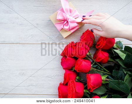 Preparing A Gift, On A Wooden Table, With Roses. Female Hand Holding A Gift, Wrapped With Ribbon, On