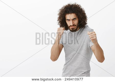 Indoor Shot Of Outraged Bully With Beard And Afro Haircut, Standing In Boxing Pose With Raised Clenc