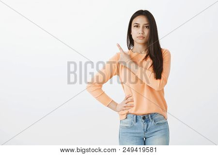 Indoor Shot Of Intense Unhappy Aduly Woman With Dark Straight Hair, Holding Hand On Hip And Pointing