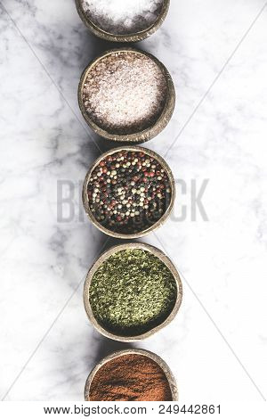 Set Of Spices On Rustic Murble Background. Coconut Shell Bowls With Paprika Salt Parsley And Pepper.