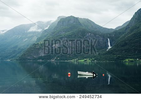 Norwegian landscape with mountain and Feigumfossen waterfall. White boat in the Lusterfjord fjord. Summer day. Commune Luster, Norway