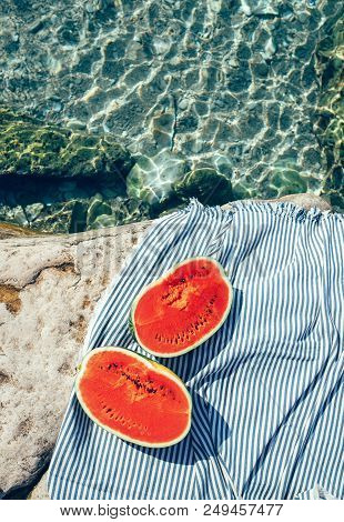 Two Watermelon Halfs Are On Striped Carpet. Sea Lagune With Clear Water, Rocky Bank