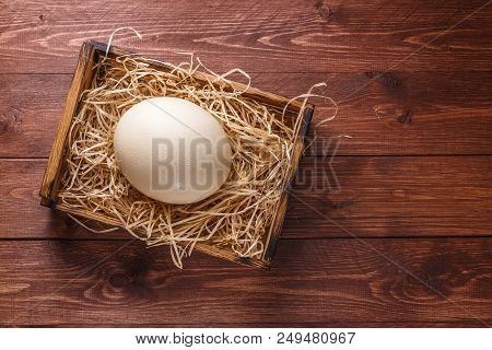 Ostrich Egg On Straw In Wooden Box, Copyspace, Dark Background.