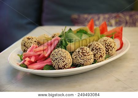 Falafel Balls Covered In Sesame In A Platter Along With The Traditional Accompanying Vegetables.