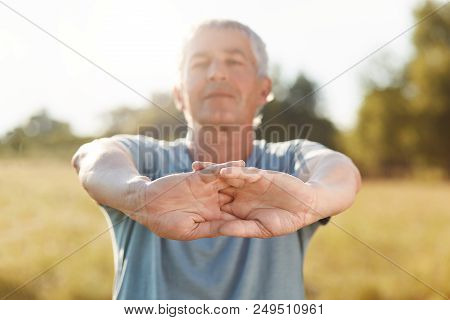 Horizontal Shot Of Handsome Active Mature Male Stretches Hands, Does Physical Exercise Outdoor, Feel