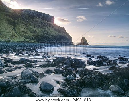 Beautifully Shaped Black Boulders And A Dramatic Fiery Sunset And A Stony Beach