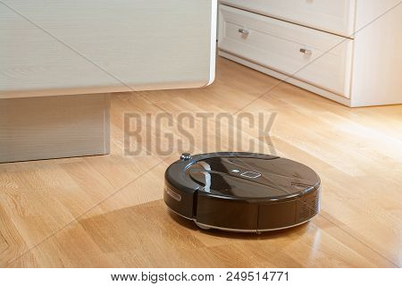 Robot Vacuum Cleaner Runs Under Bed In Bedroom In The Rays Of The Morning Sun.