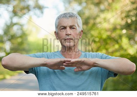 Horizontal Shot Of Confident Male Pensioner Has Outdoor Workout, Warms Up Before Jogging, Stretches 