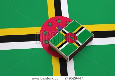 Dominica Flag  Is Pictured On A Matchbox That Lies On A Large Flag.