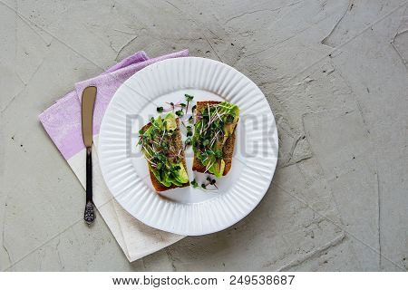 Flat-lay Of Avocado Toasts On White Plate With Micro Greens Over Light Concrete Background, Top View