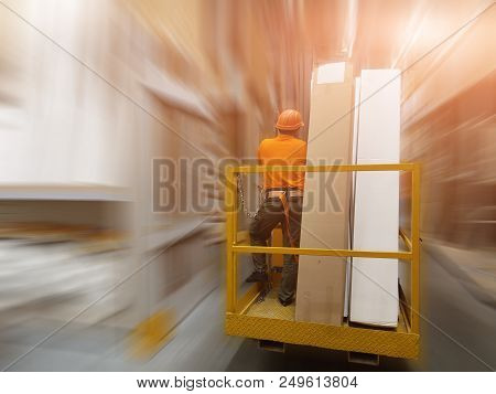 Worker In Helmet With Safety Belt On Forklift With Goods In Big Building Supermarket. Storage At War