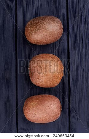 Row Of Ripe Kiwi Fruits, Top View. Three Brown Kiwi Fruits On Dark Wooden Background, Vertical Image