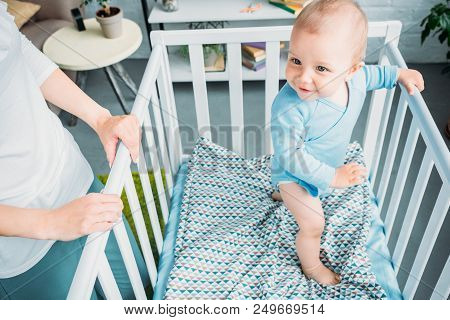 Cropped Shot Of Mother Standing Near Child In Crip At Home