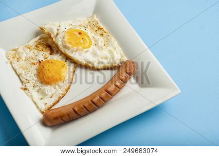 Traditional Clasic Breakfast Fried Eggs And Sausage On A White Square Porcelain Plate.