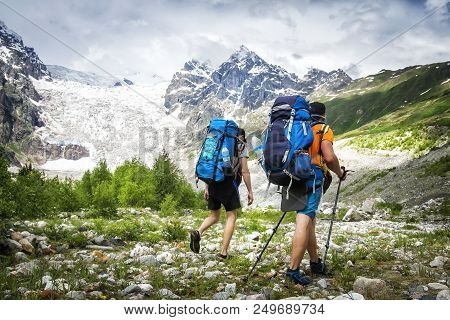 Two Hikers With Large Backpacks In Mountains. Tourists Hike On Rocky Mounts. Leisure Activity On Mou