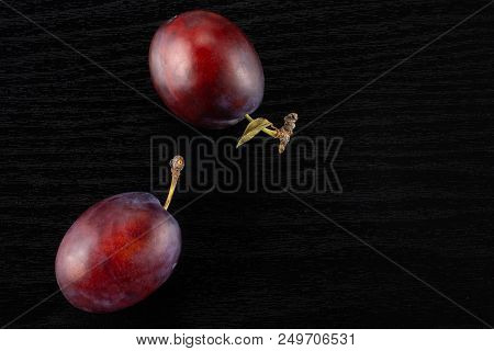 Group Of Two Whole Fresh Violet-blue Plum Vibrant Moyer Variety Flatlay On Black Wood