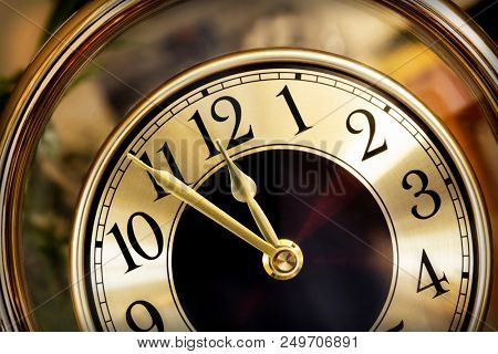 Golden clock face.  Hands showing five minutes to midnight.