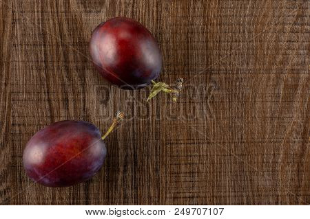 Group Of Two Whole Fresh Violet-blue Plum Vibrant Moyer Variety Flatlay On Brown Wood