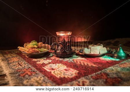 Arabian Tea In Glass With Eastern Snacks On A Carpet On Dark Background With Lights And Smoke. Easte