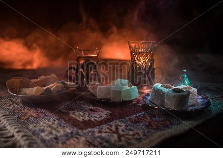 Arabian Tea In Glass With Eastern Snacks On A Carpet On Dark Background With Lights And Smoke. Easte