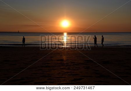 People Enjoy The Sunset At Mindil Beach. The Sun Casts Orange Shades Across An Evening Sky At Mindil