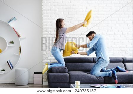 Young Hispanic Couple Sitting On Sofa At Home, Having Fun And Enjoying Quality Time. The Girl Is Pla
