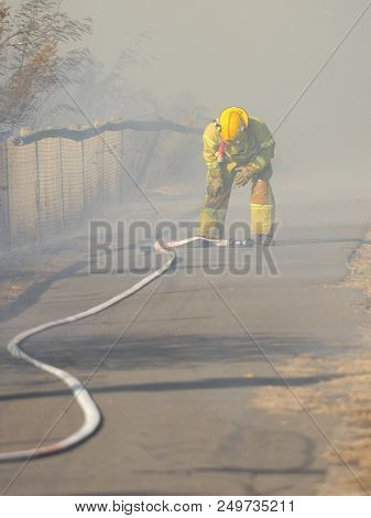 Melbourne, Australia - April 13, 2018: Fire Fighter With A Hose At A Bush Fire In An Suburban Area O