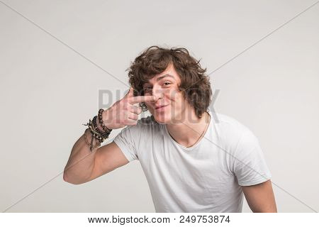 Studio Portrait Of Funny Young Man Pointing On His Nose In White T-shirt.