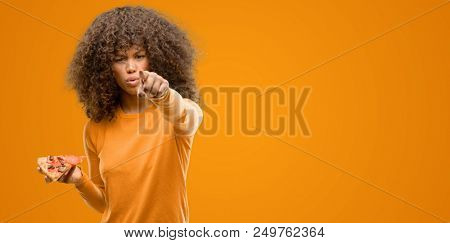 African american woman with a pizza slice pointing with finger to the camera and to you, hand sign, positive and confident gesture from the front