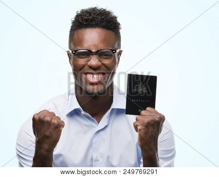 Young african american man holding australian passport screaming proud and celebrating victory and success very excited, cheering emotion