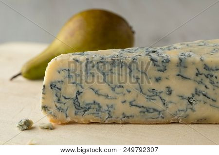 Piece of Gorgonzola picante cheese close up and a fresh ripe pear on the background for dessert