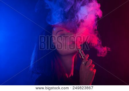 Portrait Of Asian Woman Smoking Vape Or E-cigarette In Neon Light At Black Background
