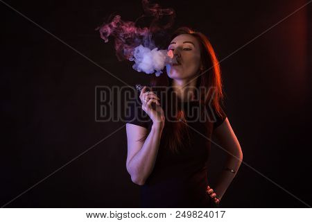 Portrait Of Asian Woman Smoking Vape Or E-cigarette In Neon Light At Black Background