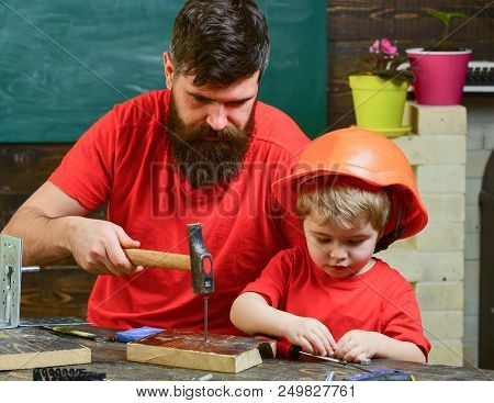 Boy, Child Busy In Protective Helmet Learning To Hammering Hobnails With Dad. Father, Parent With Be