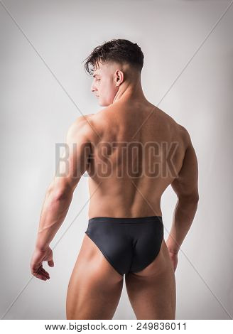 Rearview Of Young Gym Fit Man Showing His Sexy Back While Looking To A Side. On Light Background In 