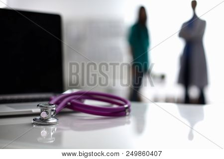 Laptop And Stethoscope On The Desk , Doctors Standing In The Background.