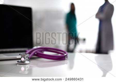 Laptop And Stethoscope On The Desk , Doctors Standing In The Background.