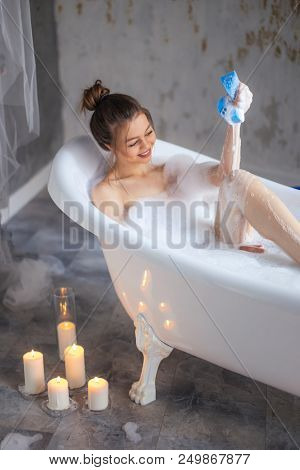 Pleasant Girl Is Plaing With Sponge In The Bathroom With Candles On The Floor