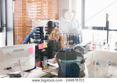 Two African Office Workers Are Proffering Help To Their Red-haired Partner In The Busy Room With Gla