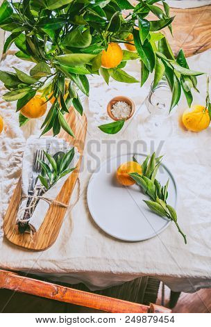 Table Setting With White Plate, Cutlery, Linen Napkin And Orange Tree Branch Decoration On White Lin