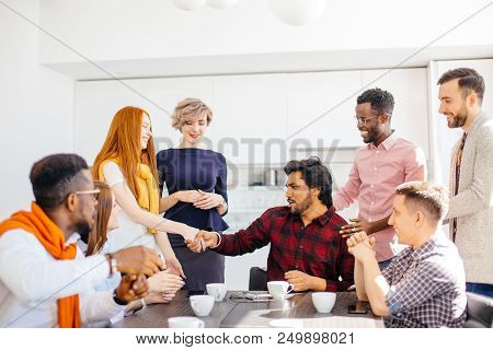 Closeup Photo Of Hindoo Employee Giving A Warm Handshake To Smiling Red-haired Woman In Front Of Co-