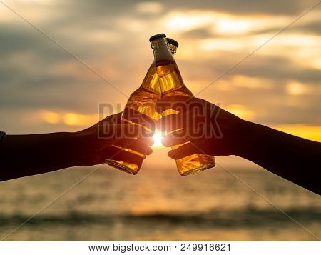 Couple Hands Holding Beer Bottles And Clanging On The Sunset Beach. Party, Holiday, Summer, Friendsh