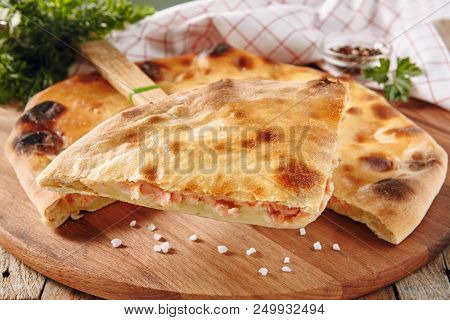 Fresh Baked Piece of Pie Stuffed with Salmon, Potato and Cheese Close Up with Selective Focus. Slice of Delicious Red Fish Tart Serving with Greens and Spices on Rustic Wooden Background