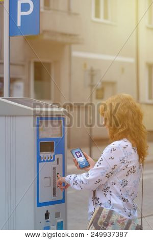 Woman using smartphone app to pay for parking in the paid parking zone in a city