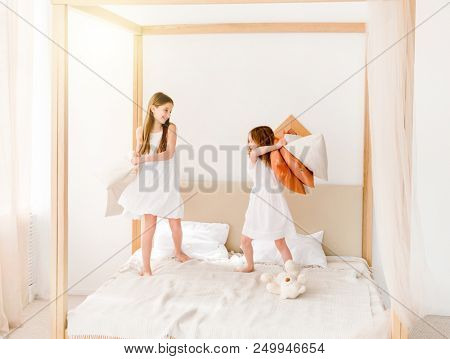 Two little girls fighting with pillows on the bed. Two sisters having pillow fight at bedroom. Sublings playing together